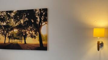 A hotel room with a large bed, a nightstand, a lamp, and a painting of trees on the wall.