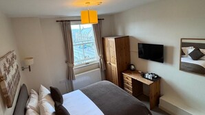 Una habitación de hotel con una cama, un escritorio, un televisor y un ventanal con cortinas.