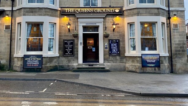 Un edificio con un letrero que dice "The Queens Ground".