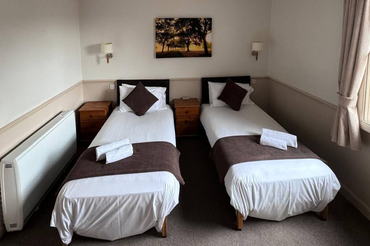 A hotel room with two single beds, a radiator, a painting on the wall, and a window with curtains.