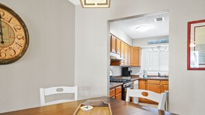 A dining area with a wooden table, two white chairs, and a wall clock. - Beachwalk Resort by Panhandle Getaways (Panama City Beach)