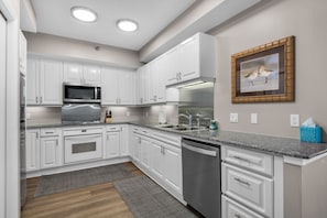 A modern kitchen with white cabinets, stainless steel appliances, and a granite countertop. - Pristine, Family-friendly condo. Spectactular Gulf Views! (Navarre)