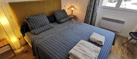 A neatly made bed with a patterned bedspread and pillows, a bedside lamp, and a window with curtains.
