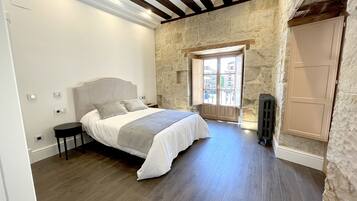 A bedroom with a bed, a nightstand, a stone wall, a window, and a radiator.