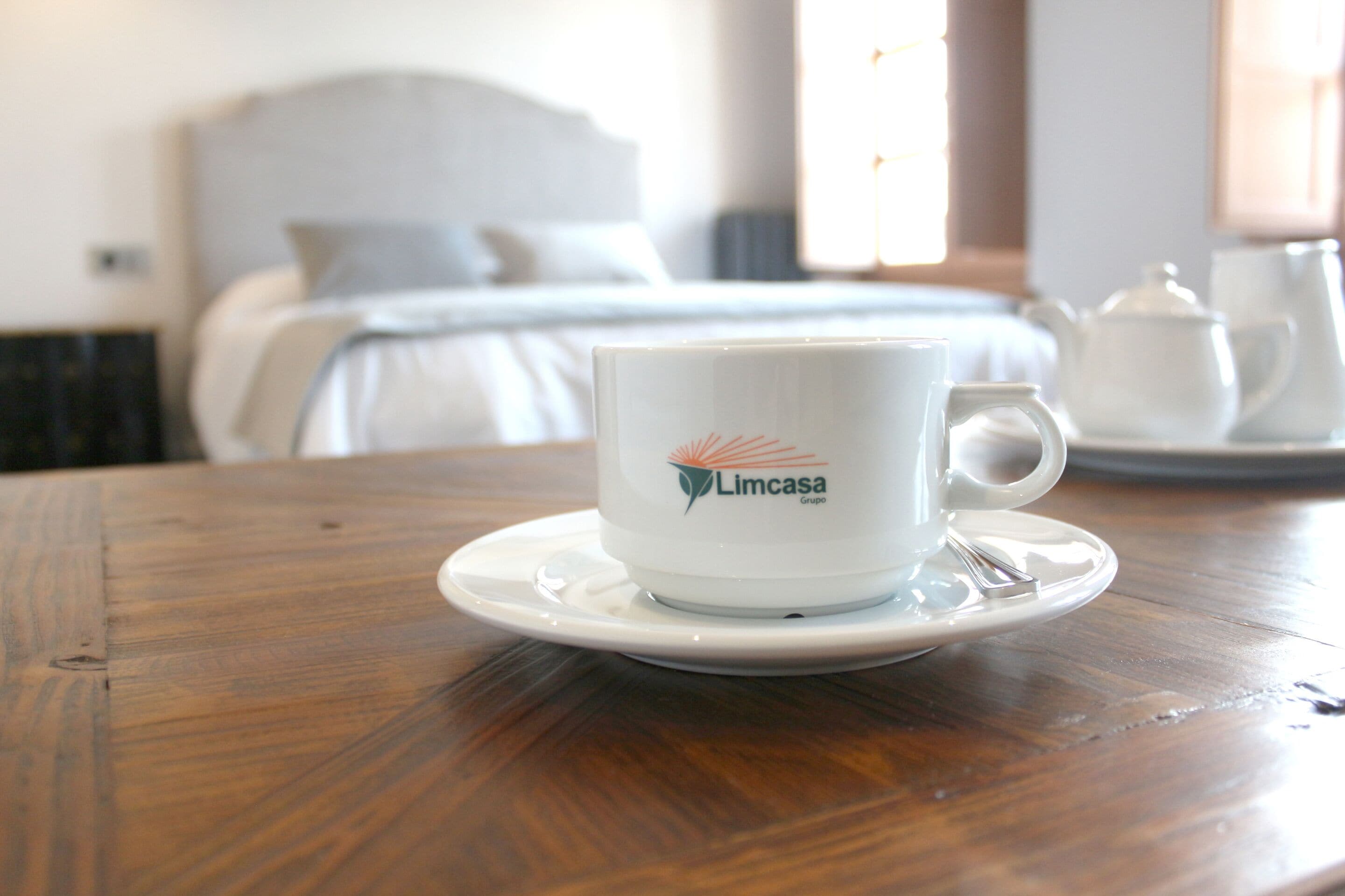 A white cup with the logo "Limcasa Grupo" on a wooden table in a hotel room.