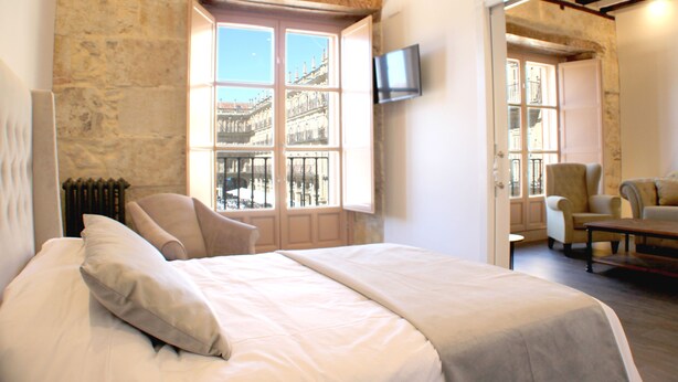 Une chambre à coucher avec un grand lit, une chaise, une table et un téléviseur fixé au mur.