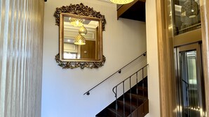 Un escalier dont les marches sont recouvertes d’un parquet disposé en point de Hongrie, menant à un palier agrémenté d’un miroir et de luminaires suspendus.