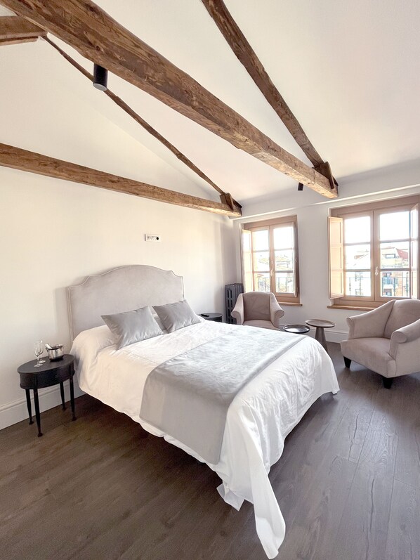 A bedroom with a large bed, a chair, a small table, and a window with a view.