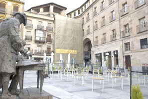 Una plaza con una escultura, mesas al aire libre y edificios históricos.