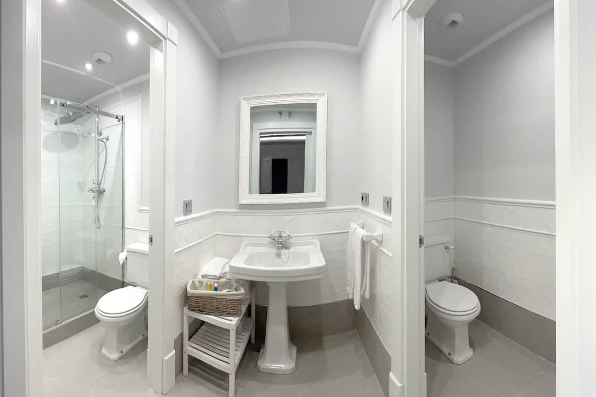 A modern bathroom with a glass-enclosed shower, a pedestal sink, and two toilets.
