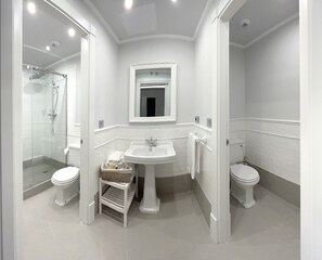 Un baño moderno con ducha de vidrio, lavamanos pedestal y dos inodoros.