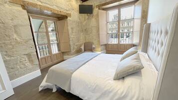 Un dormitorio con una cama grande, paredes de piedra, techo de madera y una ventana con vistas a edificios.