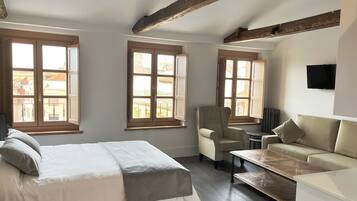 Quarto com cama, cadeira, sofá e mesa. Janelas com molduras de madeira e radiador na parede.