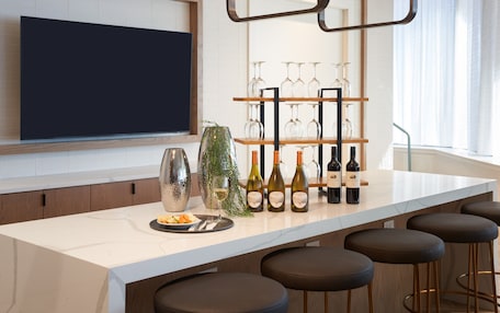 A modern kitchen with a large island, wine bottles, and glasses on shelves.
