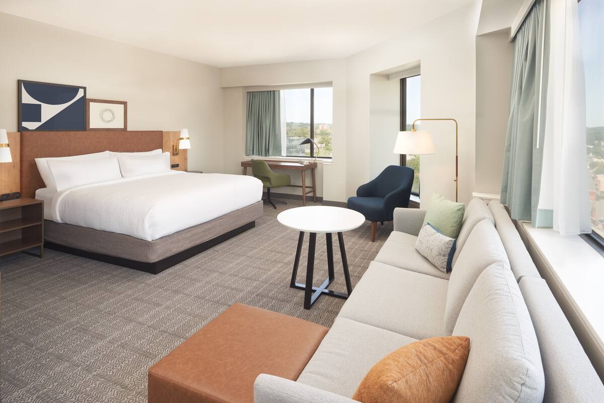 A hotel room with a large bed, a sofa, a desk, and a chair.
