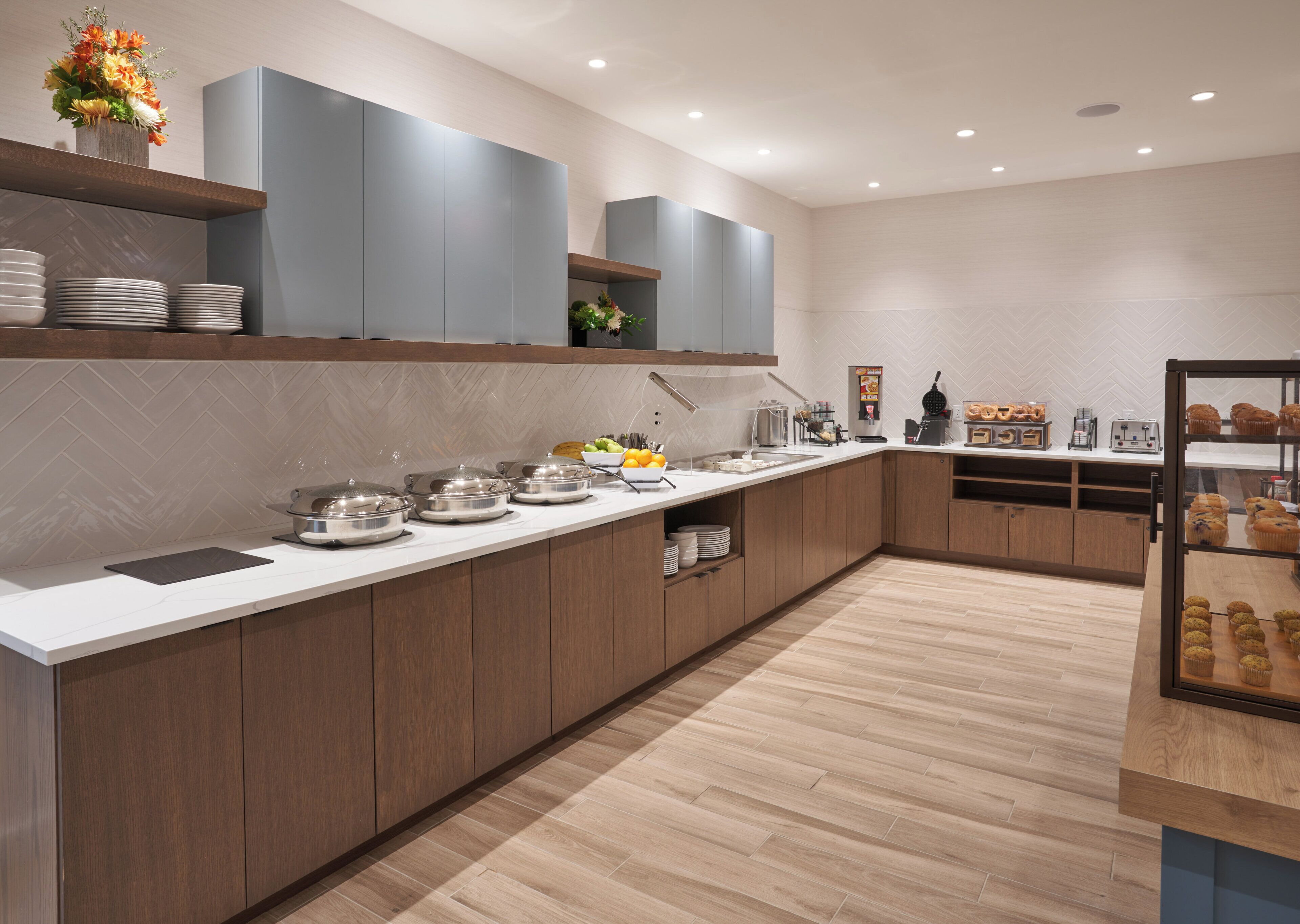A modern kitchen with a long counter, built-in cabinets, and a variety of food items.