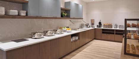 A modern kitchen with a long counter, built-in cabinets, and a variety of food items.
