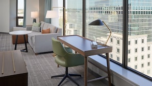 Una habitación de hotel moderna con un ventanal grande, un sofá, un escritorio y una silla.