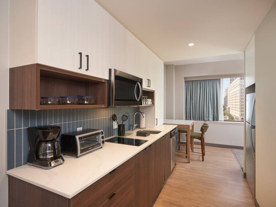 A modern kitchen with a built-in oven, microwave, and toaster. There is a window with curtains and a view of buildings outside.