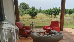 A patio with two red leather chairs, a beige ottoman, and a wooden table. There is a white lantern and a white decorative piece on the left. The patio is on a tiled floor with a view of a vineyard in the background. - Villa Domus Nirale, 4 km from Civita di Bagnoregio, panorama of Lake Bolsena. (Bagnoregio)