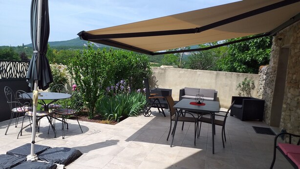 Un patio al aire libre con una mesa y sillas, un paraguas grande y un muro de piedra.