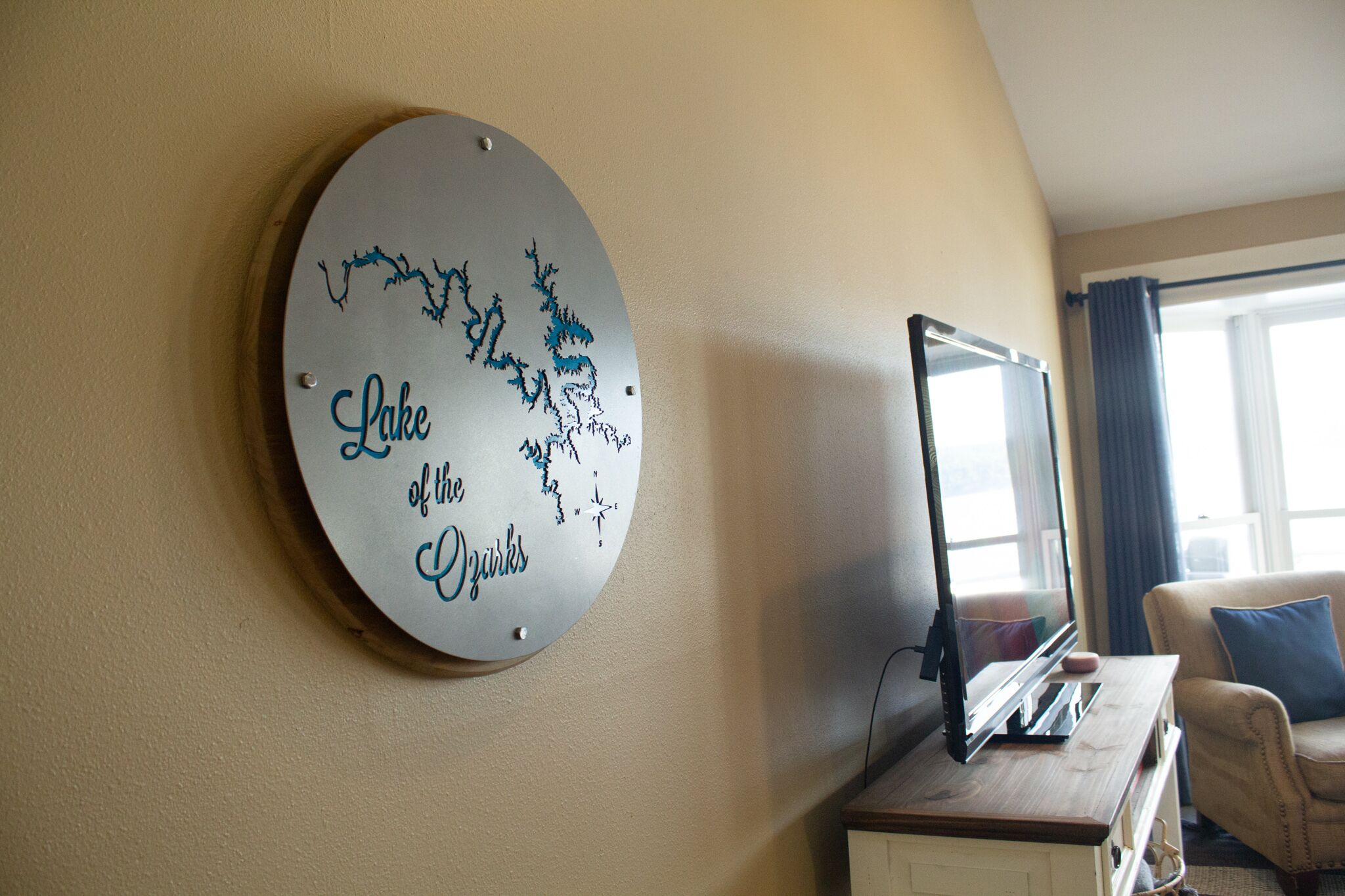 A round wall decoration with a map and text, a flat-screen TV, a wooden desk, and a beige armchair in a room with beige walls.
