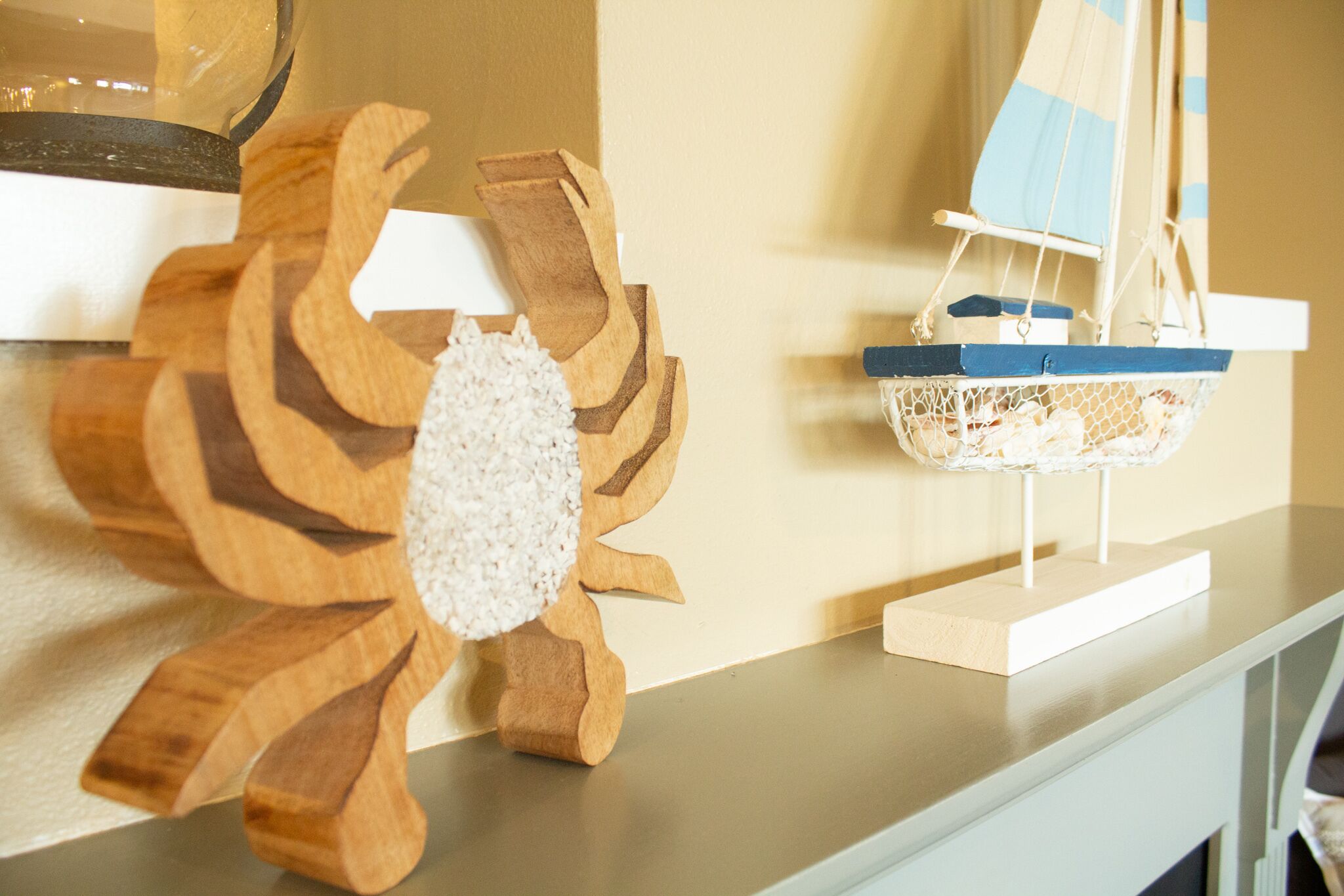 A wooden decorative piece resembling a flower with a textured center, a small sailboat model, and a white shelf.