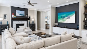 A modern living room with a fireplace, a large flat-screen TV, and a ceiling fan.
