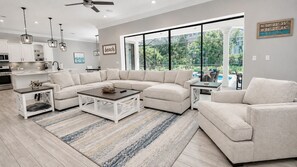 Un salon moderne avec un canapé d’angle, une table basse et une grande fenêtre donnant sur un paysage verdoyant.