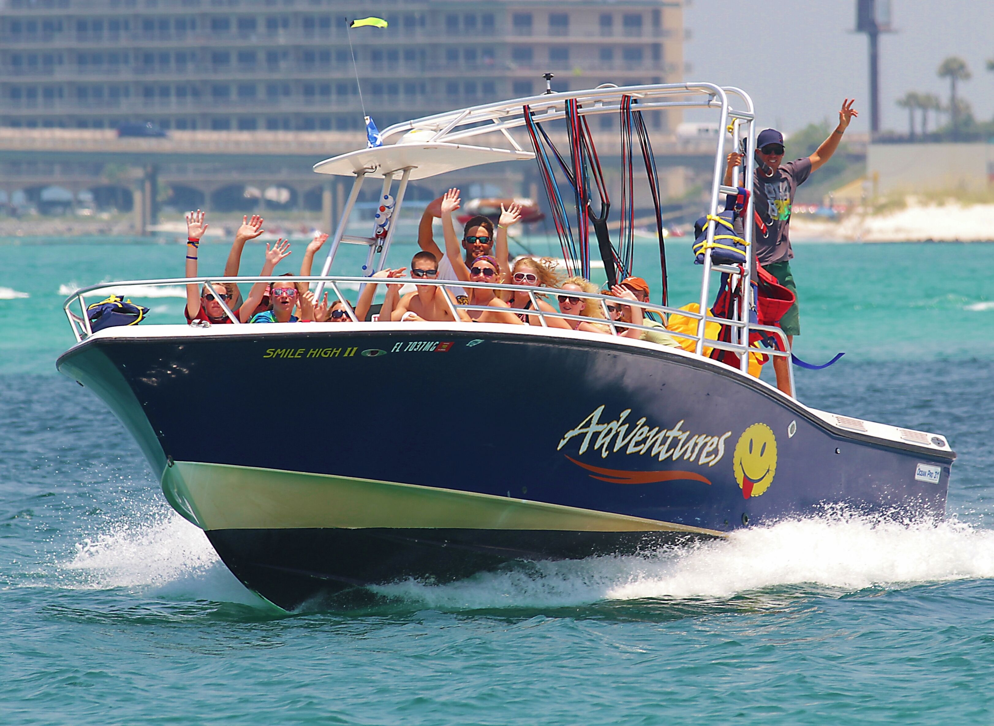 A boat with the name "Adventures" on its side, moving through water with passengers raising their hands.