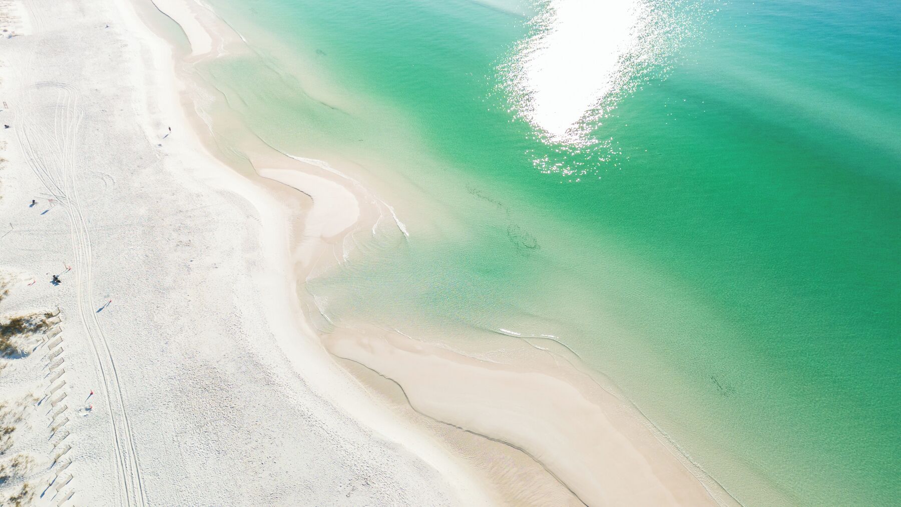 An aerial view of a beach with clear turquoise water, white sand, and visible footprints.