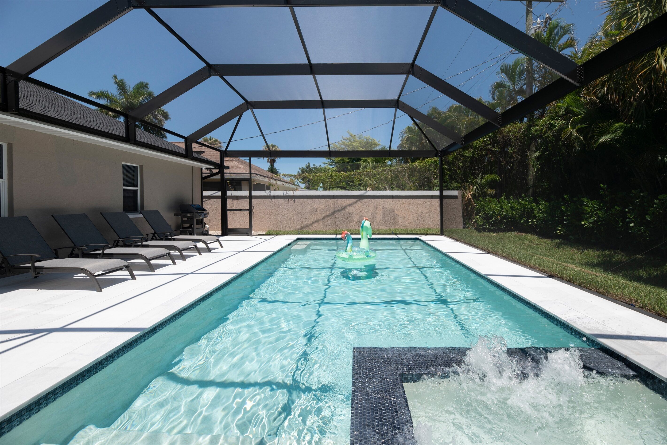 A swimming pool with a glass enclosure, surrounded by lounge chairs and a patio area.