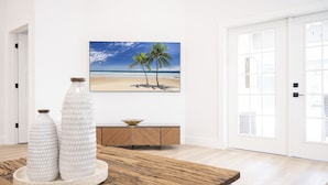 Ein Essbereich mit einem Holztisch, zwei weißen Vasen, einer Holzkommode und einem Gemälde mit Strandmotiv an der Wand.