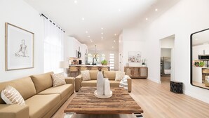 Ein großzügiger Wohnbereich mit einem Holztisch, beigen Sofas und einer Küche im Hintergrund.