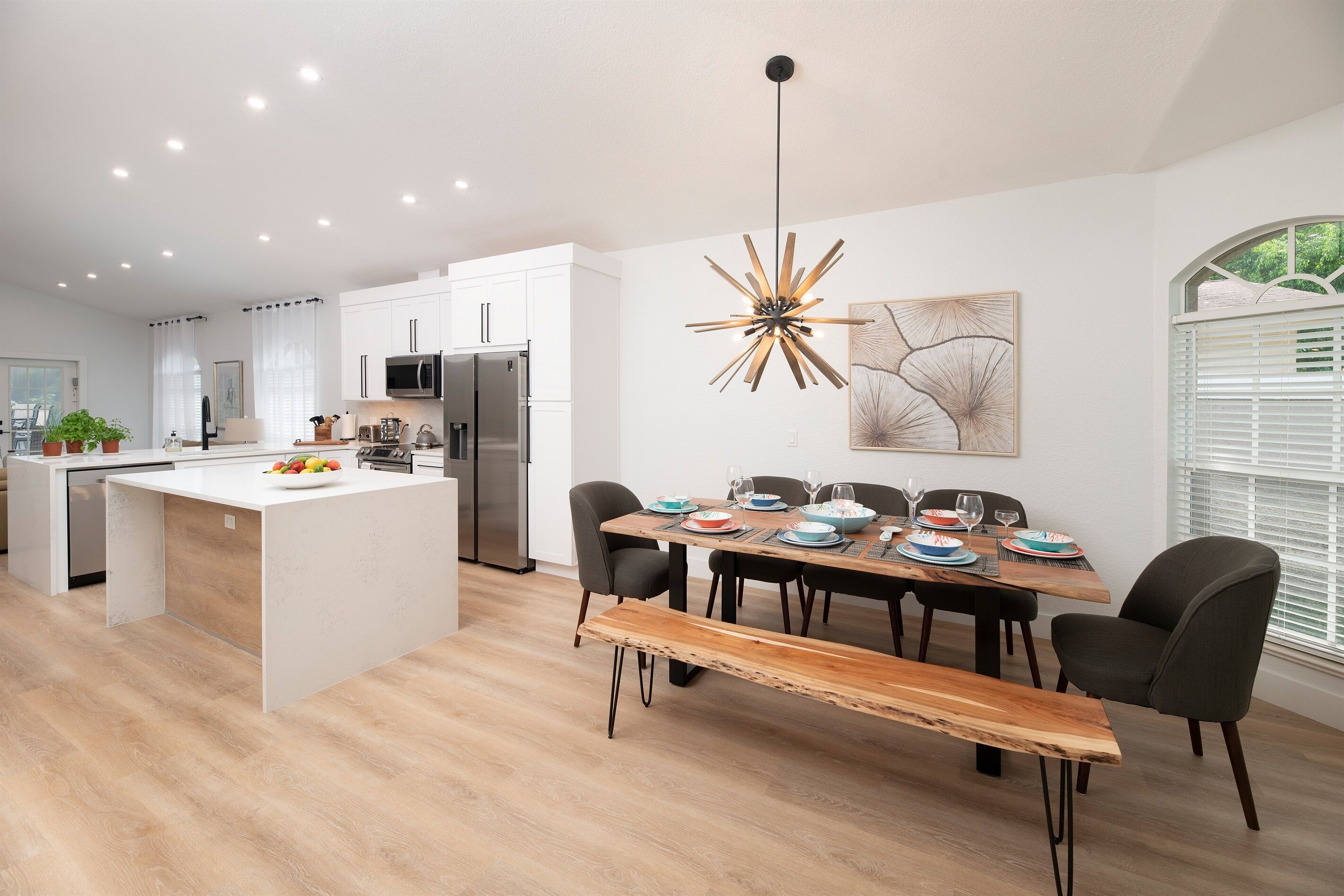 A modern kitchen with white cabinetry, a central island, and a dining area with a wooden bench.