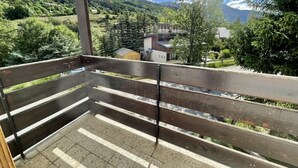 Een balkon met uitzicht op een bergachtig landschap, een houten bankje en een metalen hekwerk.