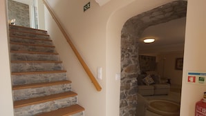 Una escalera de piedra con barandillas de madera que conduce a una sala de estar con un arco de piedra y un extintor en la pared.