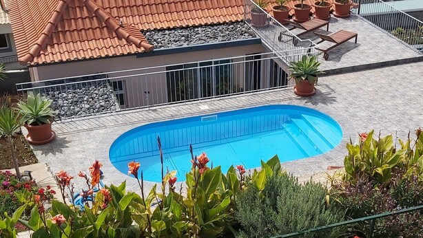 Una propiedad residencial con piscina, techo de tejas y jardín con plantas en macetas.