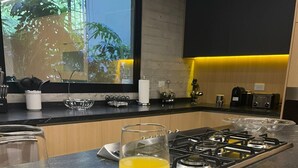 Une cuisine moderne avec une cuisinière à gaz, deux verres de jus d’orange sur un plateau et une fenêtre donnant sur des arbres.