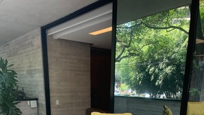 Une table ronde en bois, préparée pour le petit-déjeuner, avec des chaises à coussins jaunes, des assiettes blanches, des tasses et un plateau de fruits.