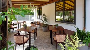 An outdoor patio area with wooden tables and chairs, potted plants, and a covered ceiling structure. - Maison des Roses (Cesenatico)