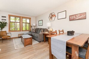 A living room with a sofa, a dining table, and a kitchen area. - The Powder Nook | Hot Pools | Mile 1 Express Chair (Panorama)