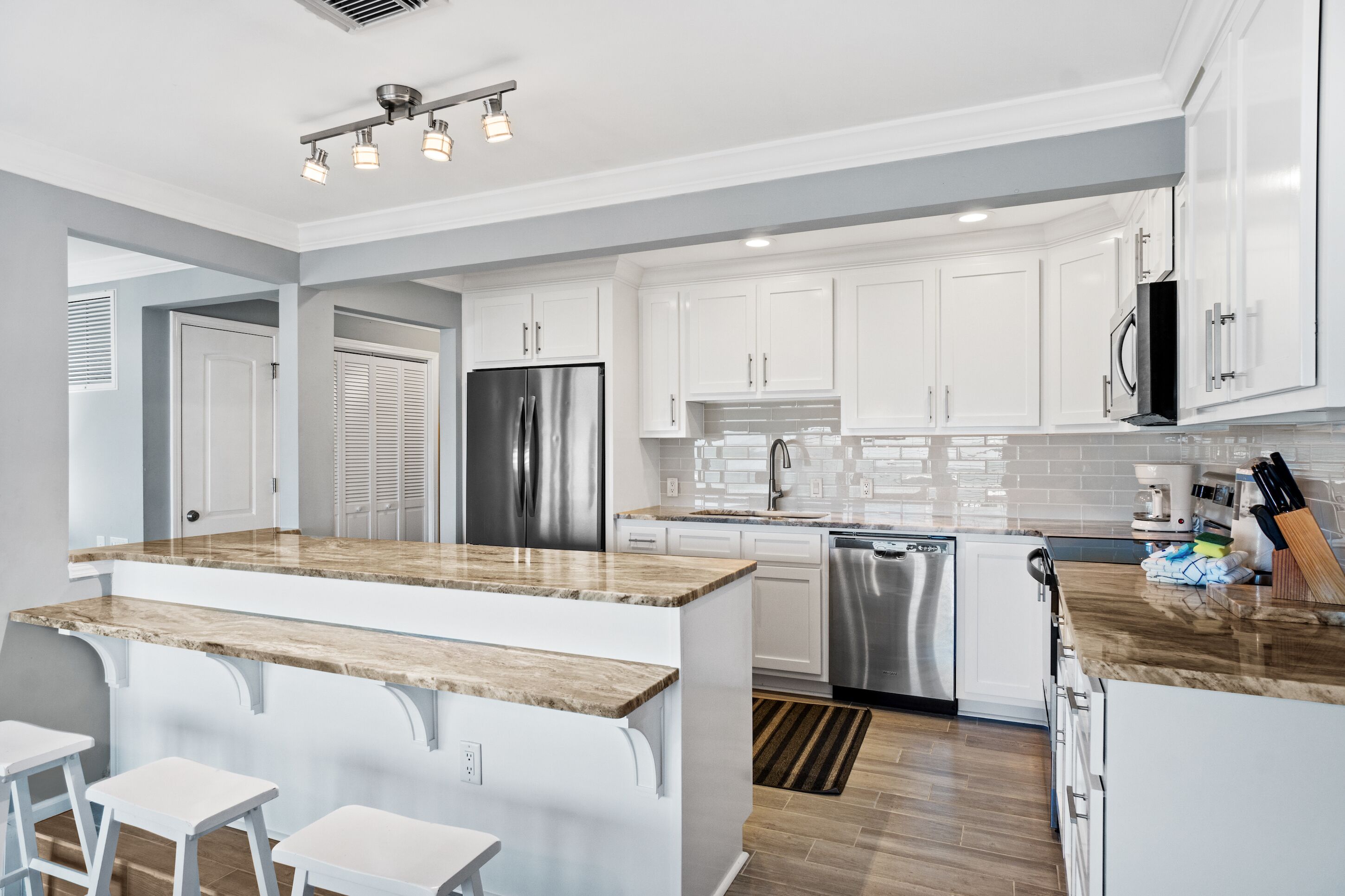 A modern kitchen with white cabinets, stainless steel appliances, and a marble countertop.