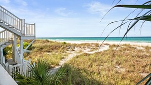 Une vue sur la plage avec un escalier en bois menant à une terrasse, le tout entouré d’herbe et de sable.