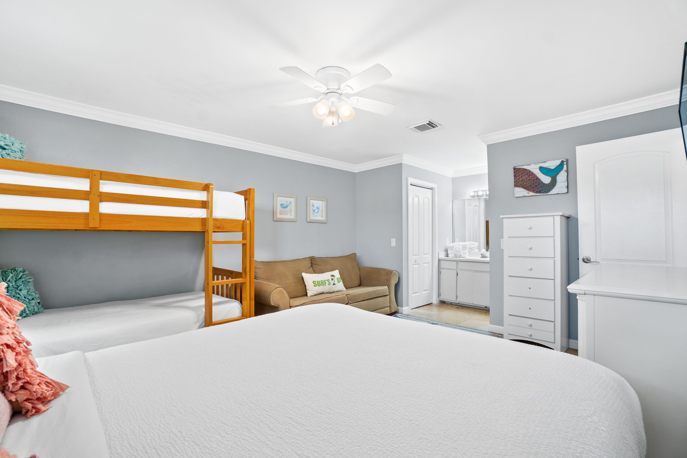 A bedroom with bunk beds, a sofa, a dresser, and a ceiling fan.