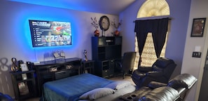 A modern bedroom with a bed, a massage chair, a TV mounted on the wall, and a bookshelf.
