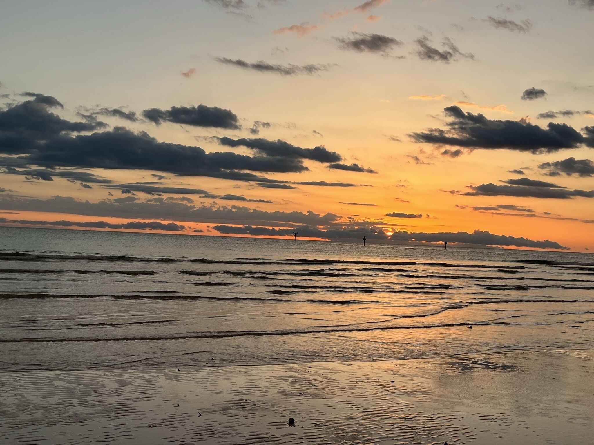 Une plage au coucher du soleil, avec des vagues et un ciel nuageux.