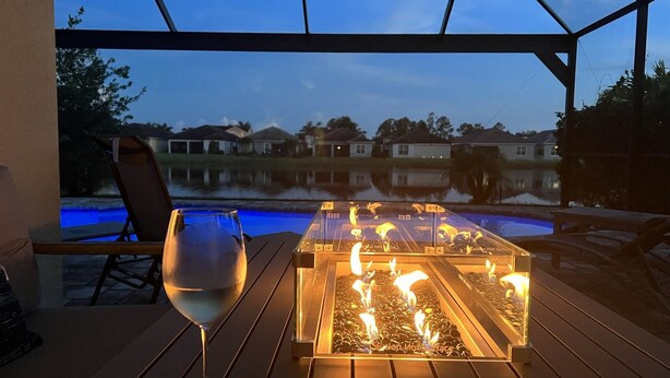 En uteplats med ett bord med glasskiva, ett glas vin och en eldstad.