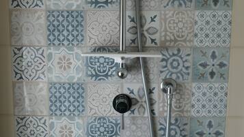 Une douche équipée d’un pommeau de douche à main et d’un pommeau de douche fixe au plafond, le tout installé devant un mur recouvert de carreaux à motifs.