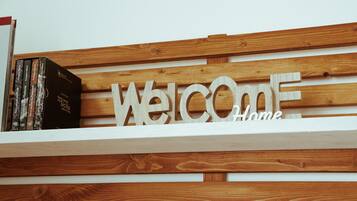 Parede de madeira com um letreiro que diz 'Welcome Home' e uma estante com livros.